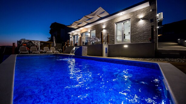 A modern hotel with a swimming pool, outdoor seating, and a well-lit facade. - Villa Hedonist (Seget)