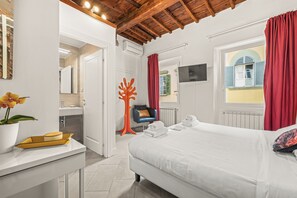 A bedroom with a bed, a desk, a chair, a window with curtains, and a view of a building outside. - Canto dei Servi (Florence)