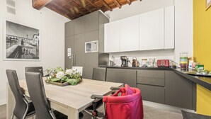 A modern kitchen with white cabinets, a microwave, and a coffee machine. There is a dining table with chairs and a red bag. - Canto dei Servi (Florence)
