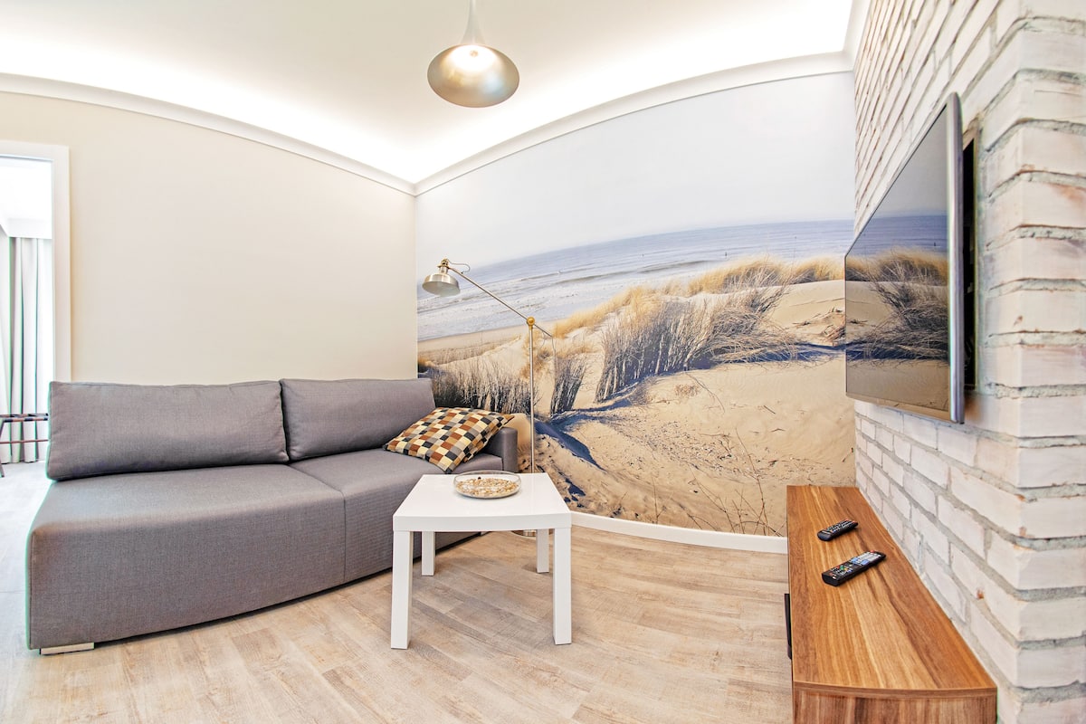 Een moderne woonkamer met een grijze bank, een witte salontafel en een houten bijzettafeltje.