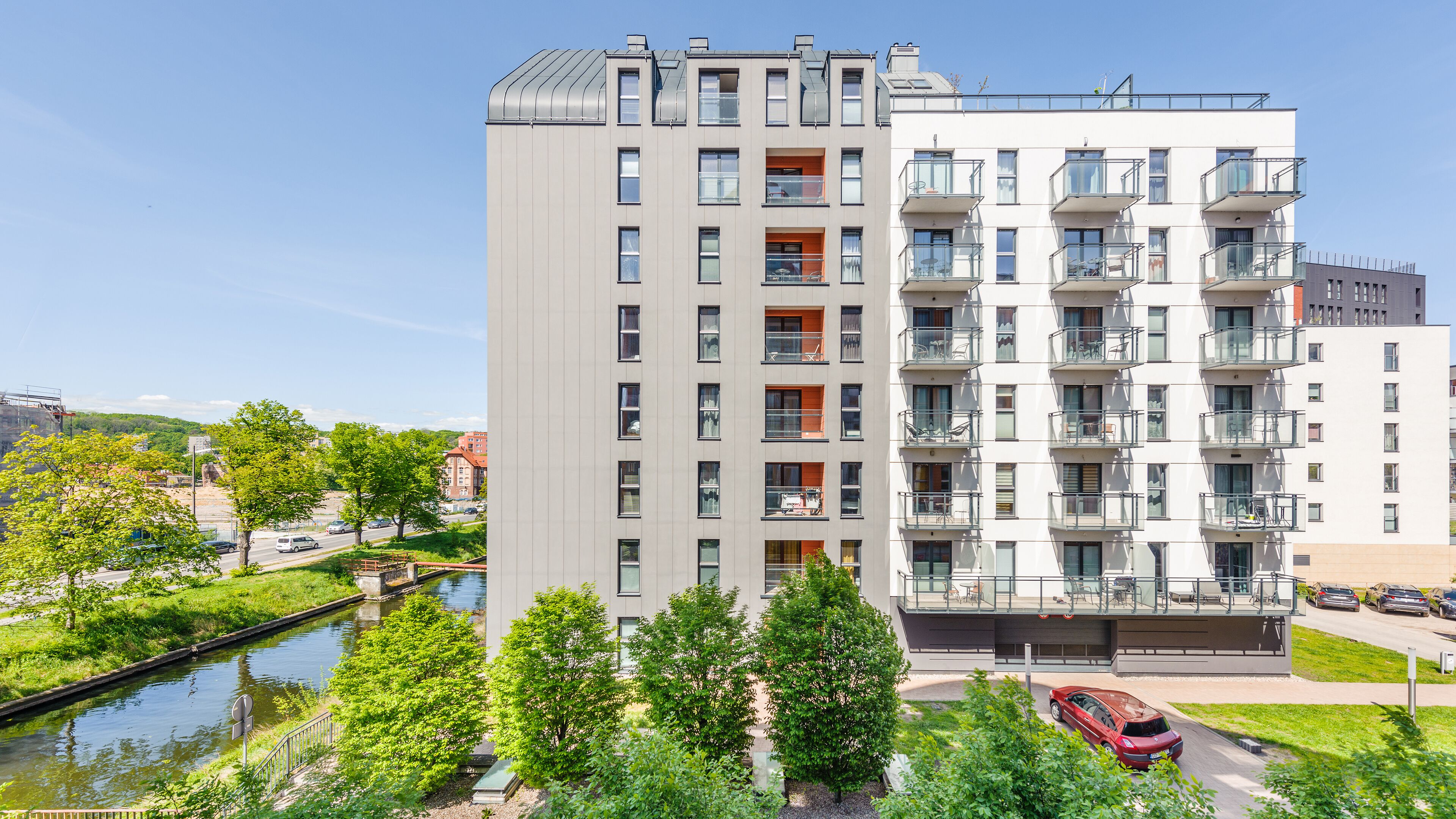 Un edificio residencial de varios pisos con balcones, un río al frente y un cielo despejado.