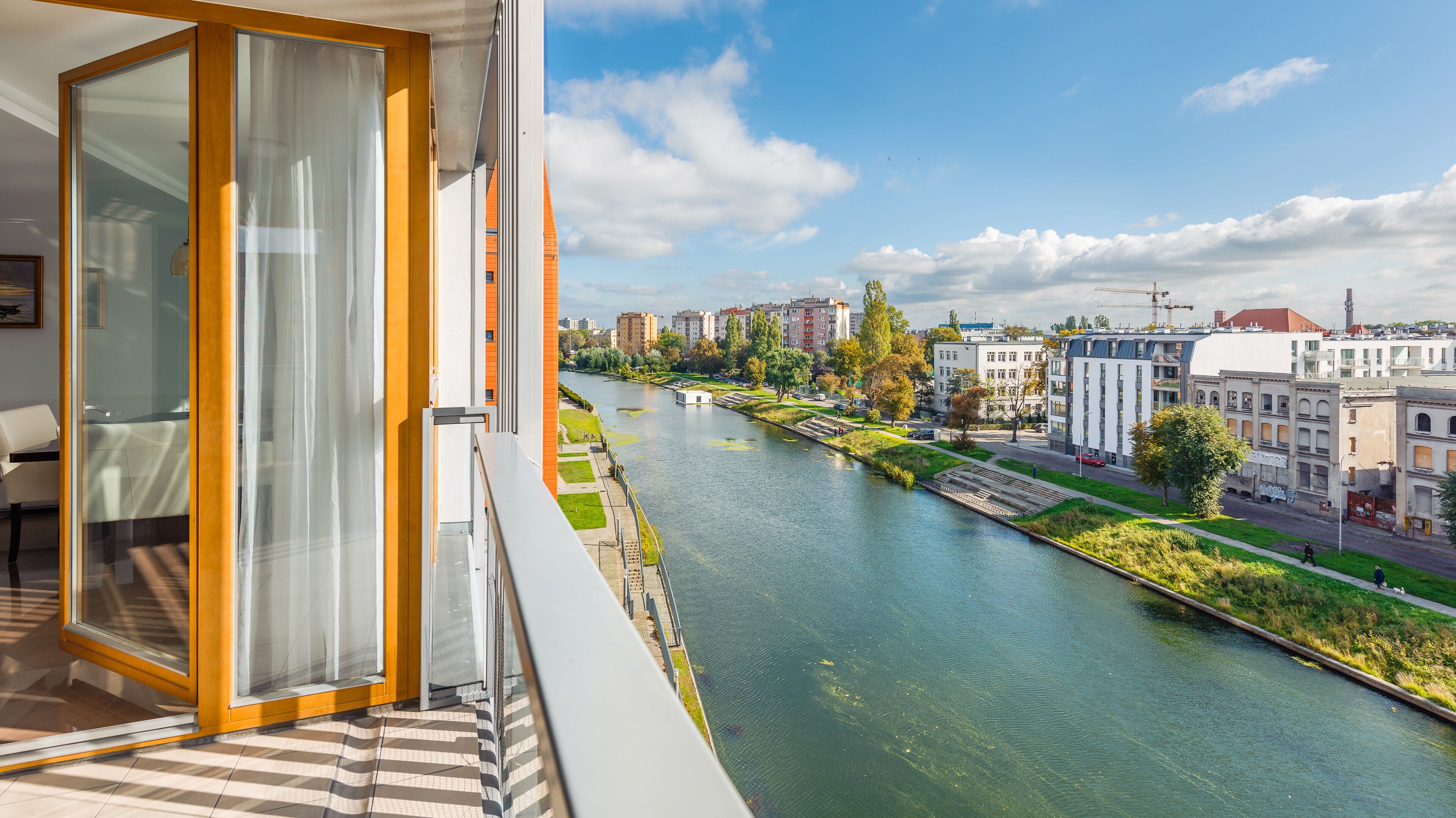 Un balcon avec vue sur une rivière, les bâtiments de la ville et un parc.
