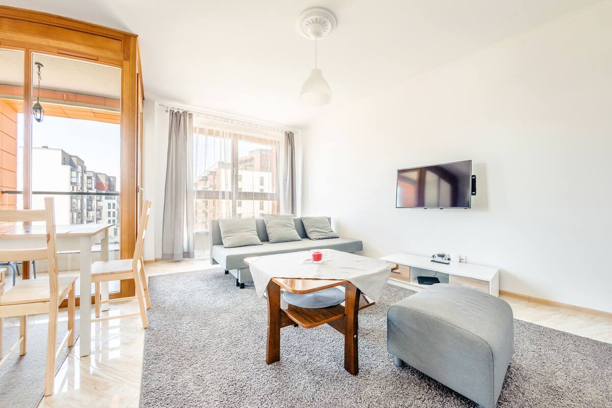 Een moderne woonkamer met een bank, een salontafel, een televisie en een eethoek met stoelen en een tafel.