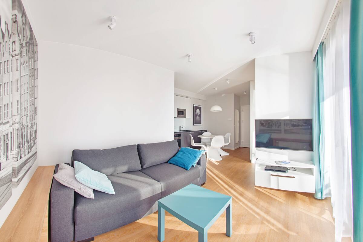 Een moderne woonkamer met een grijze bank, een kleine blauwe tafel en een tv-meubel.
