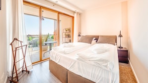 Hotellihuone, jossa on suuri sänky, yöpöytä, lamppu ja liukuovellinen lasiterassi, josta avautuu näkymä kaupunkiin.