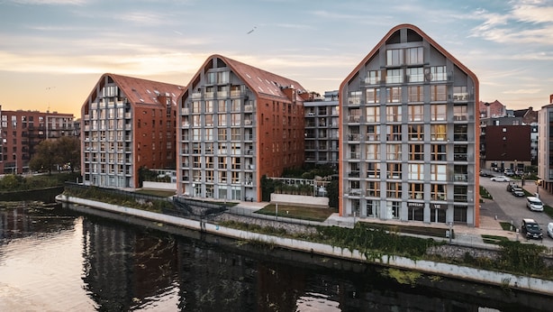 Moderni rakennus, jossa on ainutlaatuinen arkkitehtoninen ilme, suuret ikkunat ja joenäkymä.