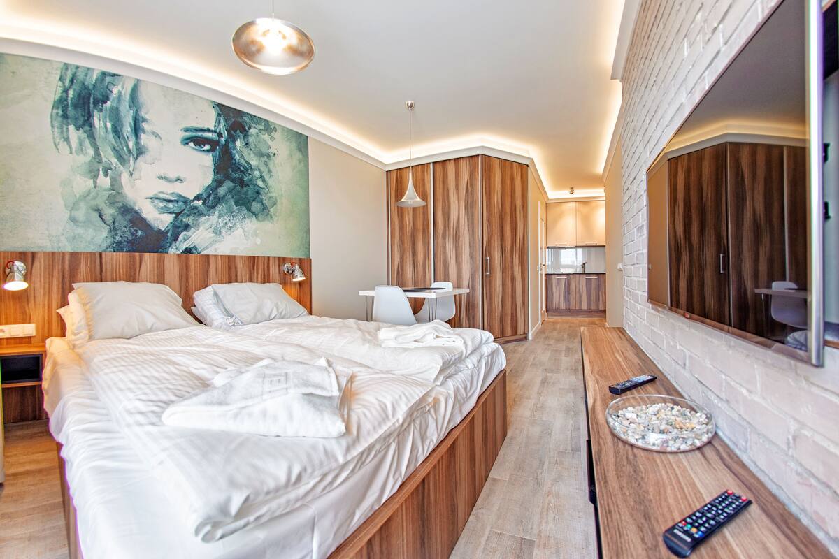 Een moderne slaapkamer met een groot bed, nachtkastjes, een bureau en een grote spiegel.