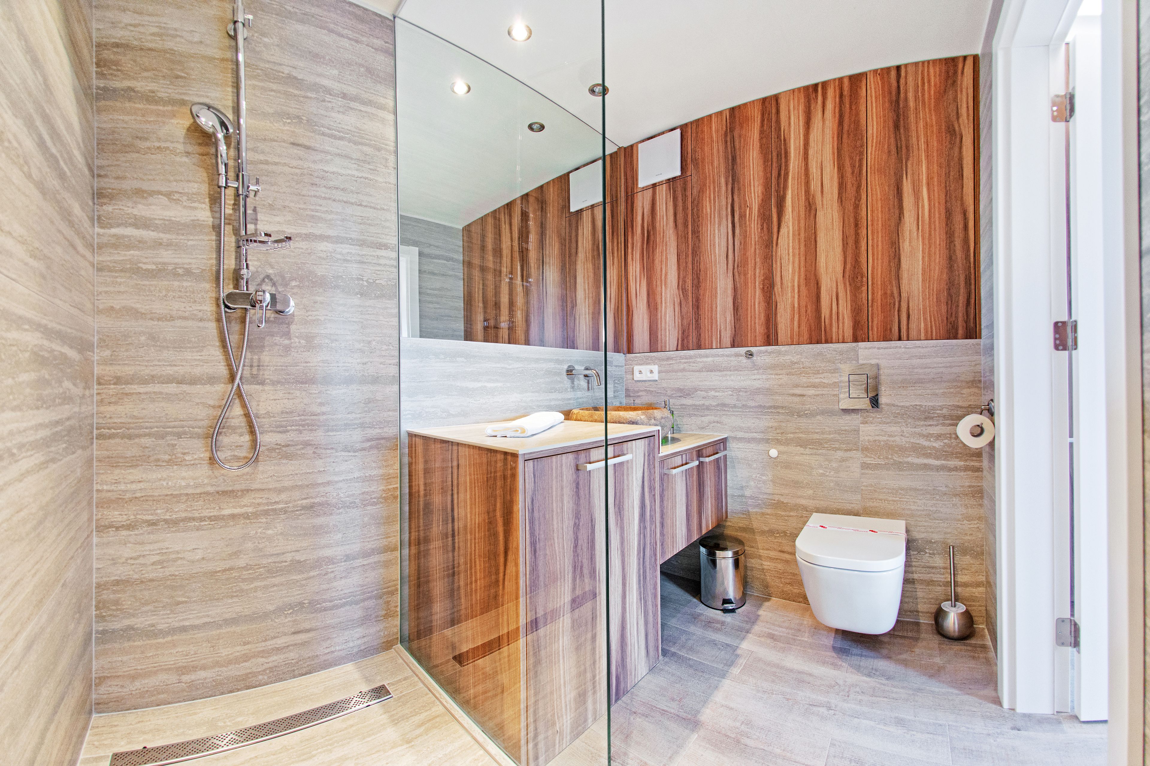 A modern bathroom with a glass-enclosed shower, a wooden vanity, and a toilet.