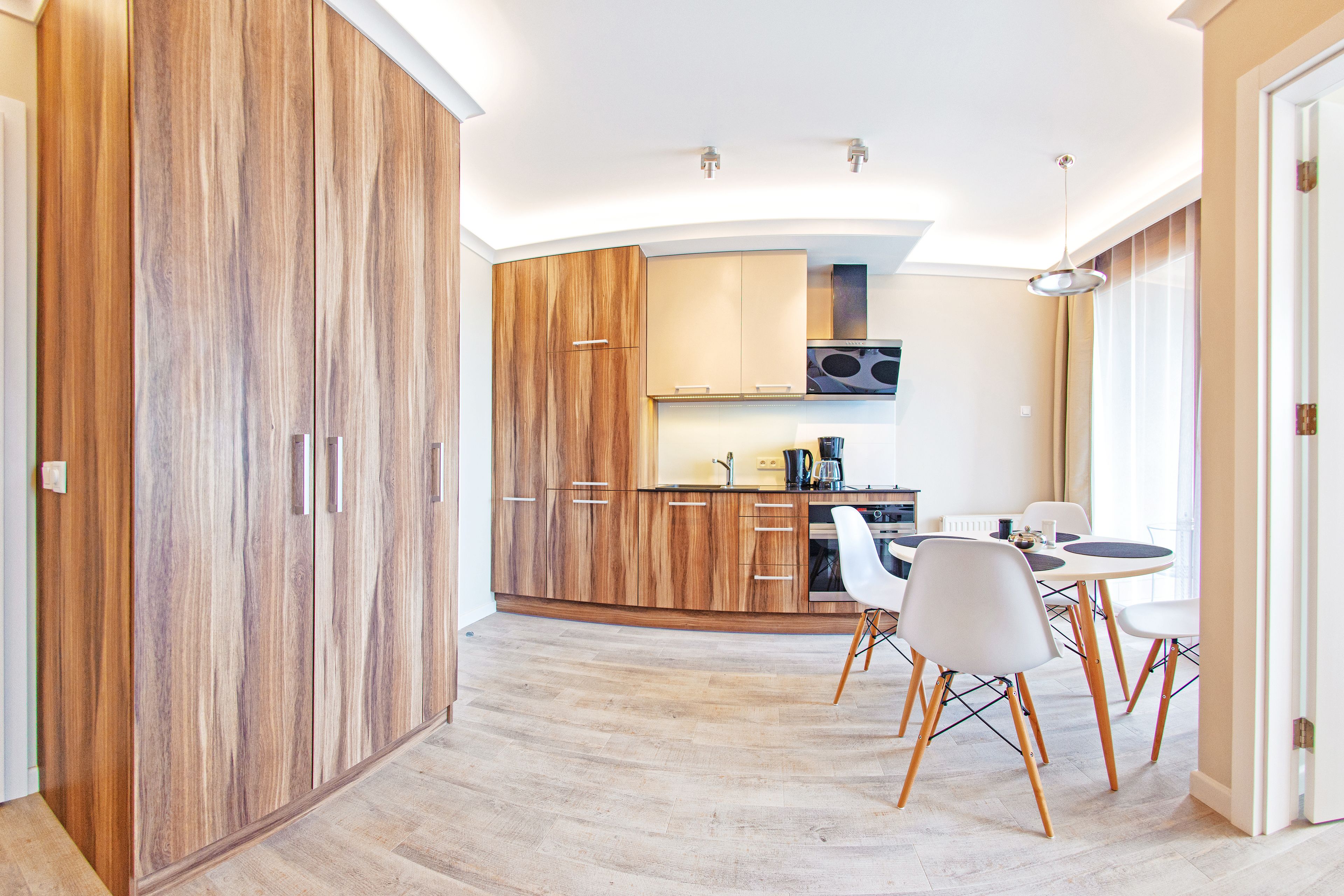 A modern kitchen with wooden cabinets, a dining area with white chairs, and a built-in oven.