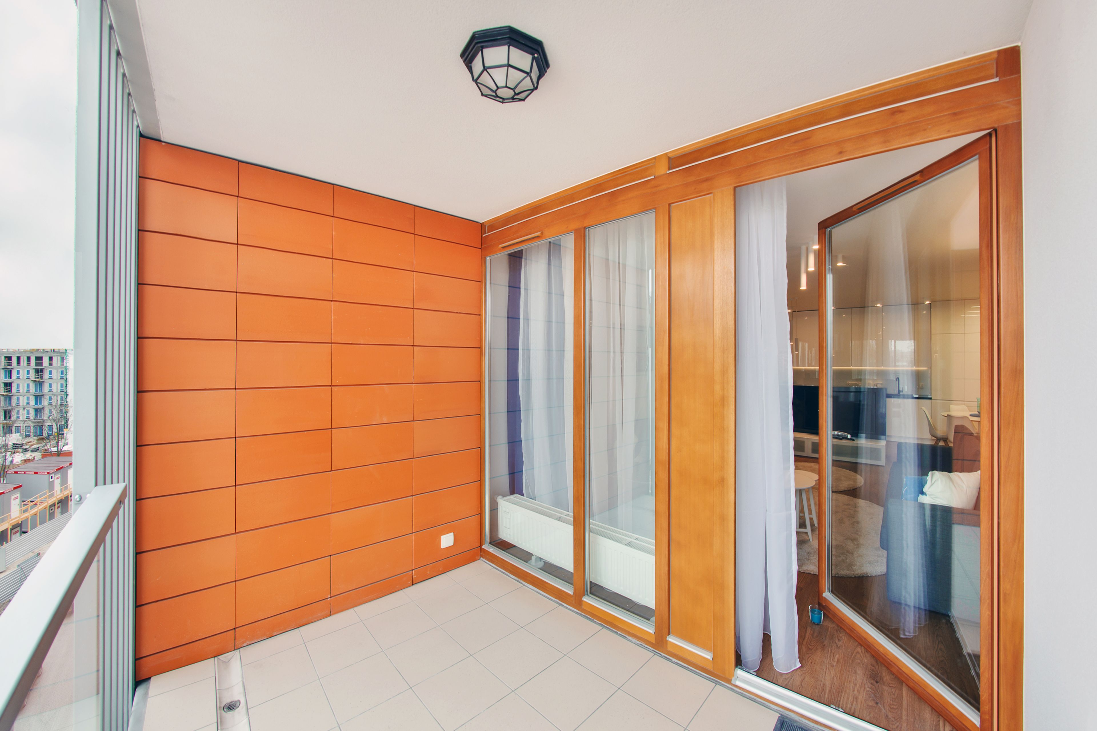 A balcony with orange paneling, a sliding glass door, and a view of the cityscape.