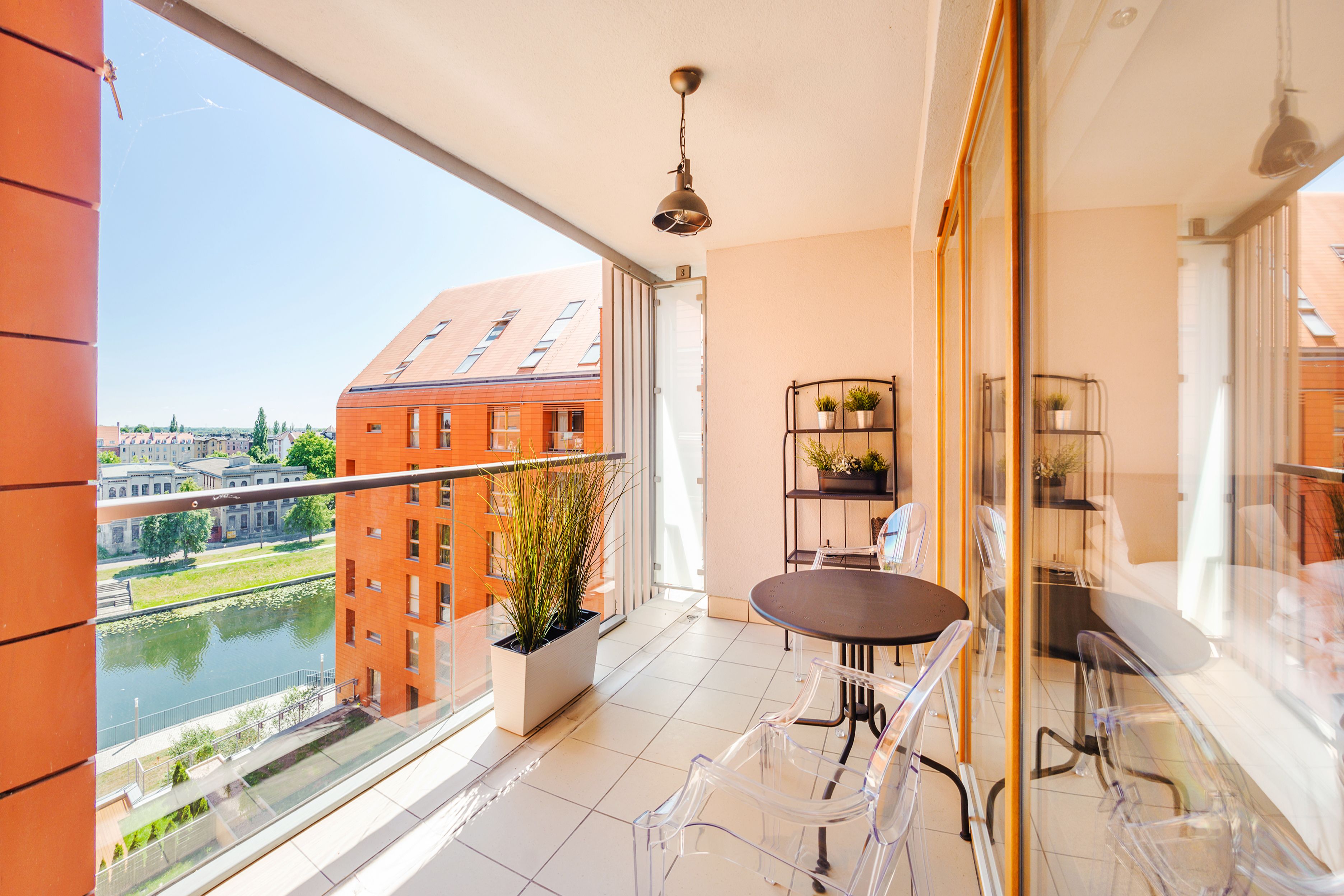Ein Balkon mit Tisch und Stühlen, einer hängenden Lampe und Blick auf einen Fluss und Gebäude.