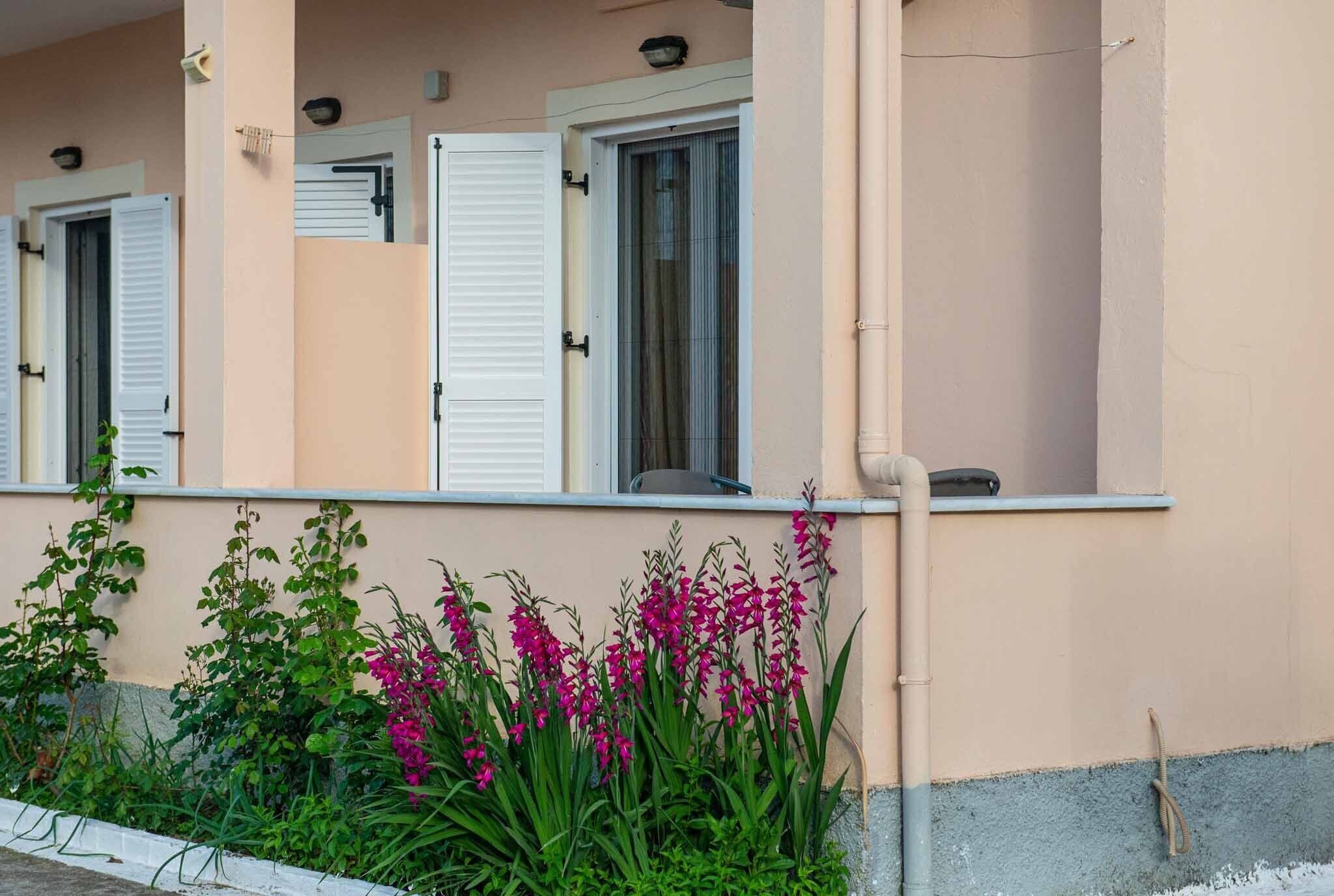 En byggnad med en persikofärgad fasad, vita fönsterluckor och en trädgård med rosa blommor.