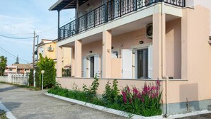 Een woonhuis met twee verdiepingen, een balkon, witte luiken en een tuin vol roze bloemen.