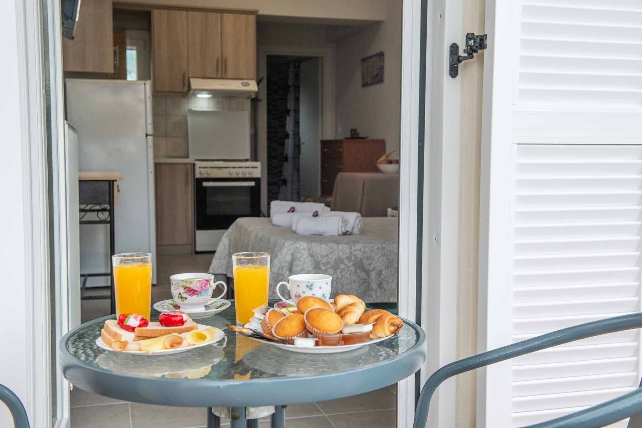 A breakfast table with toast, pastries, and orange juice in a room with a bed, a dresser, and a kitchen area.