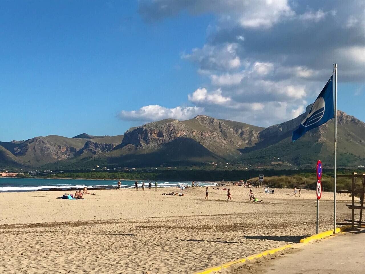 A beach with mountains in the background, a flag, and a clear sky.