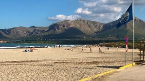 Praia com montanhas ao fundo, uma bandeira e céu claro.