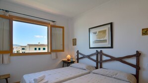 Quarto de hotel com duas camas, janela com cortinas, mesa de cabeceira com abajur e um quadro na parede.