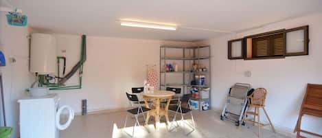 Una habitación con una mesa, sillas, una estantería con objetos y una ventana con persianas.
