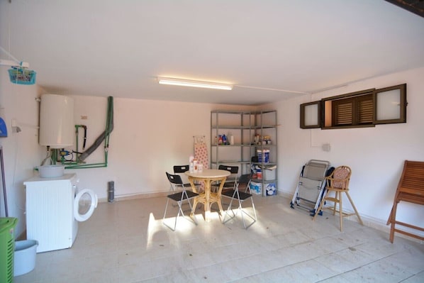 A room with a table, chairs, a shelf with items, and a window with blinds.