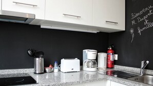A kitchen with white cabinets, a black backsplash, a coffee maker, a toaster, a kettle, a fire extinguisher, and a knife holder. - T2 suites vista rio Douro (Vila Nova de Gaia)