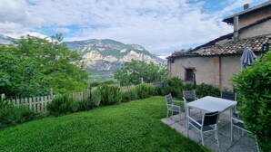 A patio with a table and chairs, surrounded by a lush green garden and a view of mountains.