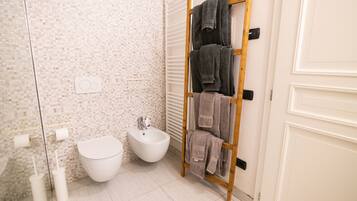 A bathroom with a bidet, two toilet paper holders, a towel rack with towels, and a white door.