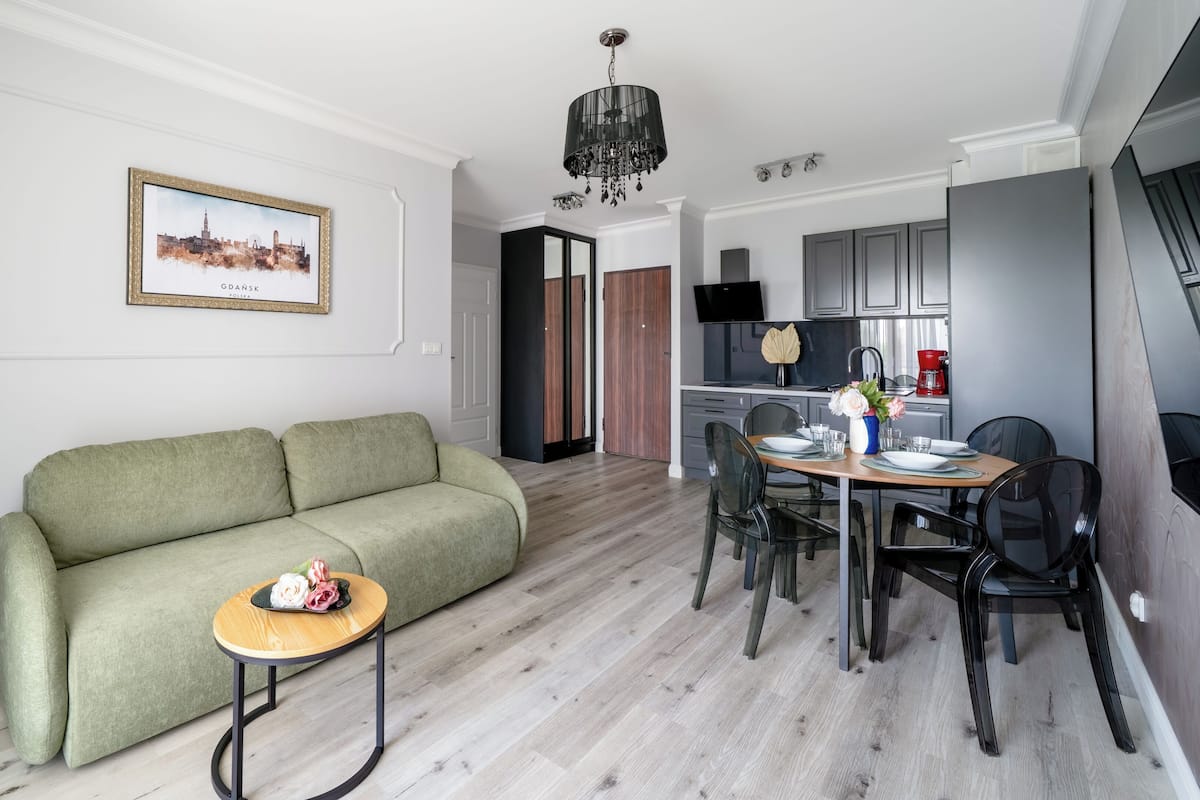 Un salon moderne avec un canapé vert, une petite table en bois et un coin repas comprenant des chaises et une table dressée pour deux personnes.