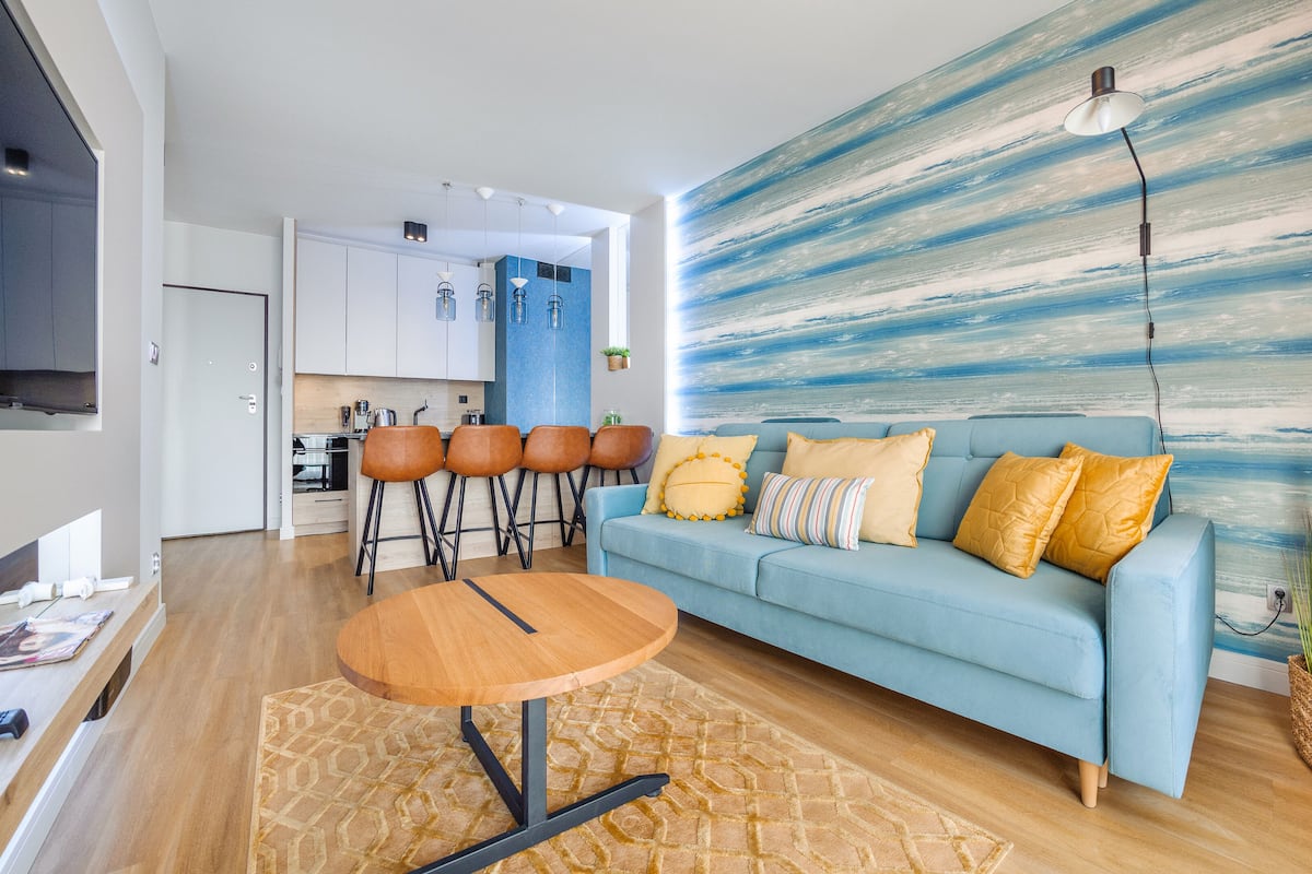 Un salon moderne avec un canapé bleu clair, une table basse en bois et un grand tableau abstrait accroché au mur.