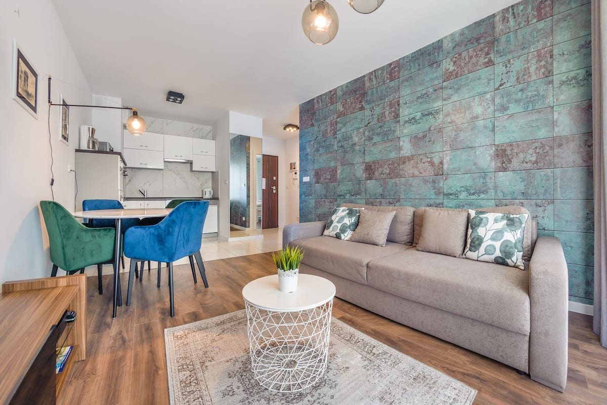 Un salon moderne avec un canapé beige, des fauteuils bleus, une table basse ronde et une cuisine en arrière-plan.