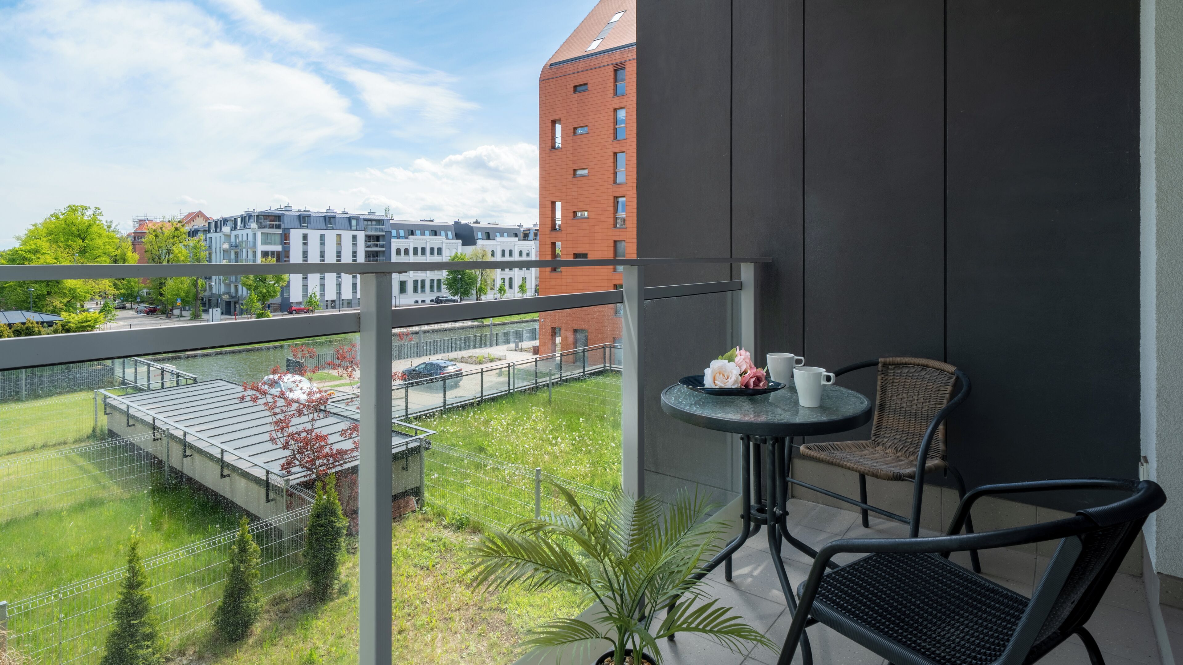 Een balkon met een tafel, stoelen en uitzicht op een rivier en gebouwen.