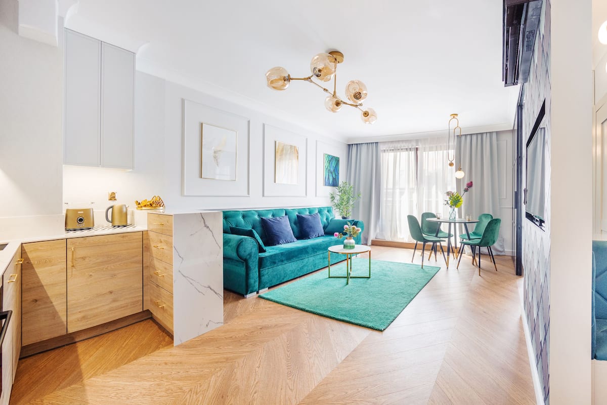 Un salon moderne avec un canapé de couleur turquoise, un meuble en bois, un séparateur en marbre et un coin repas avec des chaises vertes et une table.