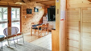 A wooden cabin interior with a dining area, a kitchen, and a large window.