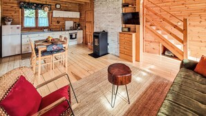 A cozy cabin interior with a wooden dining area, a sofa, a fireplace, and a staircase.