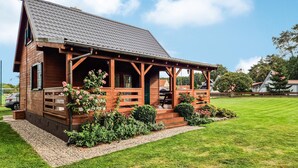 A wooden cabin with a porch, surrounded by well-maintained gardens and a lawn.