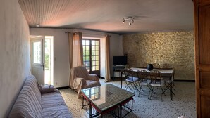 Habitació amb un sofà, una taula de dinar amb cadires, una televisió i una paret de pedra.