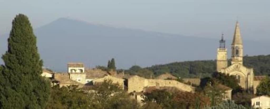 A historic town with a prominent church featuring a tall bell tower, surrounded by traditional buildings and a mountain in the background.