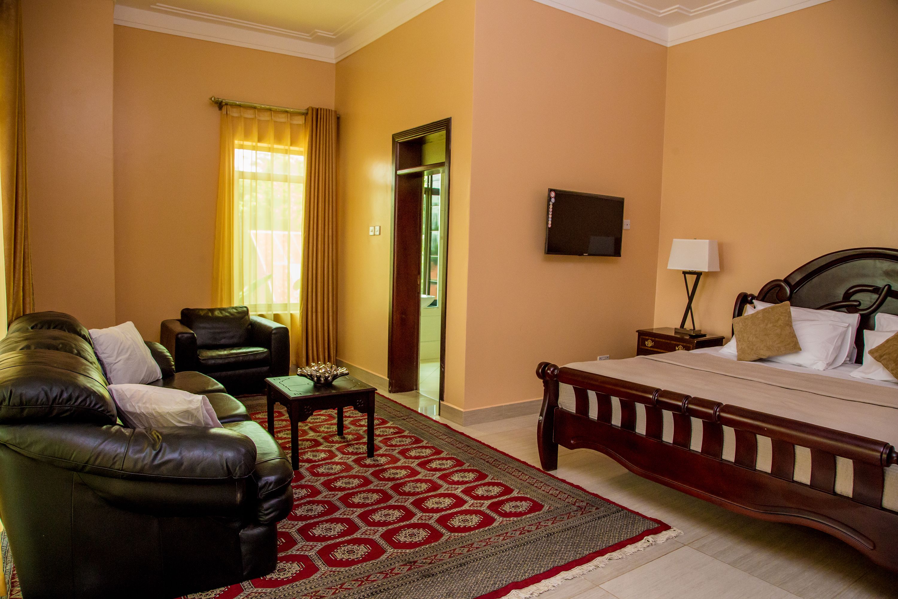 A hotel room with a bed, a sofa, a TV, and a door leading to a bathroom.