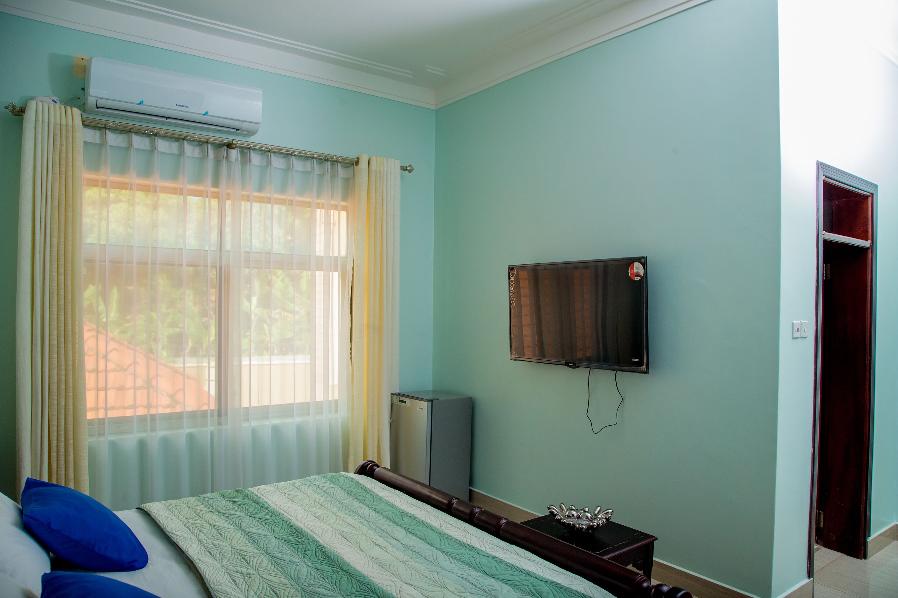 A bedroom with a bed, a TV mounted on the wall, and a window with curtains.