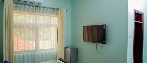 A bedroom with a bed, a TV mounted on the wall, and a window with curtains.