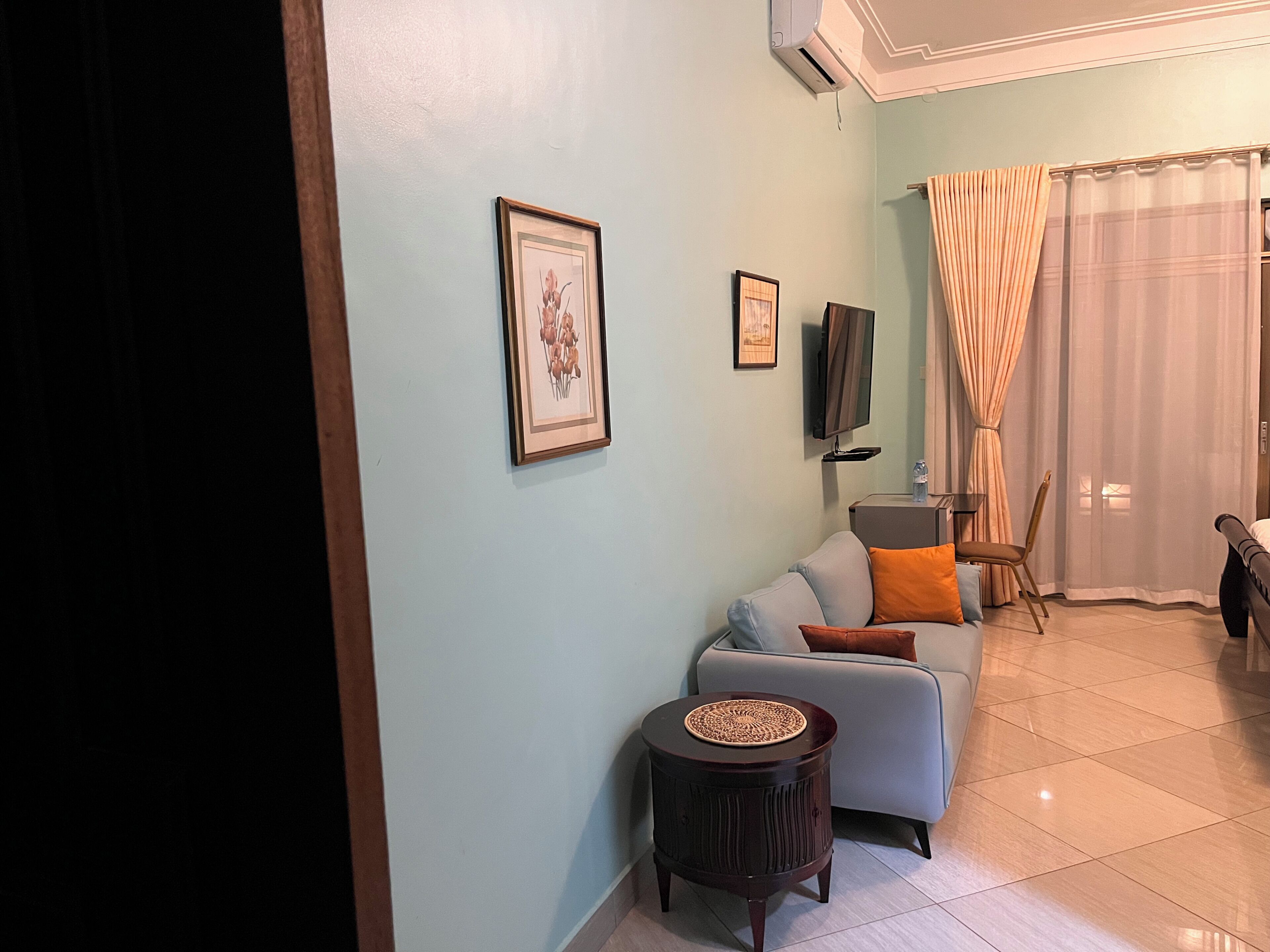 A living room with a sofa, a small round table, a television, and a window with curtains.