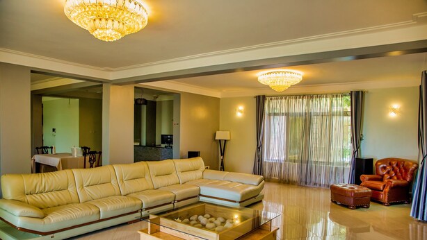 A spacious living room with a large beige sectional sofa, a glass coffee table with decorative items, a red leather armchair, and a chandelier.