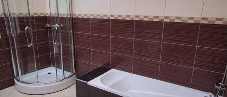 A bathroom with a glass-enclosed shower, a white bathtub, and dark brown tiled walls.