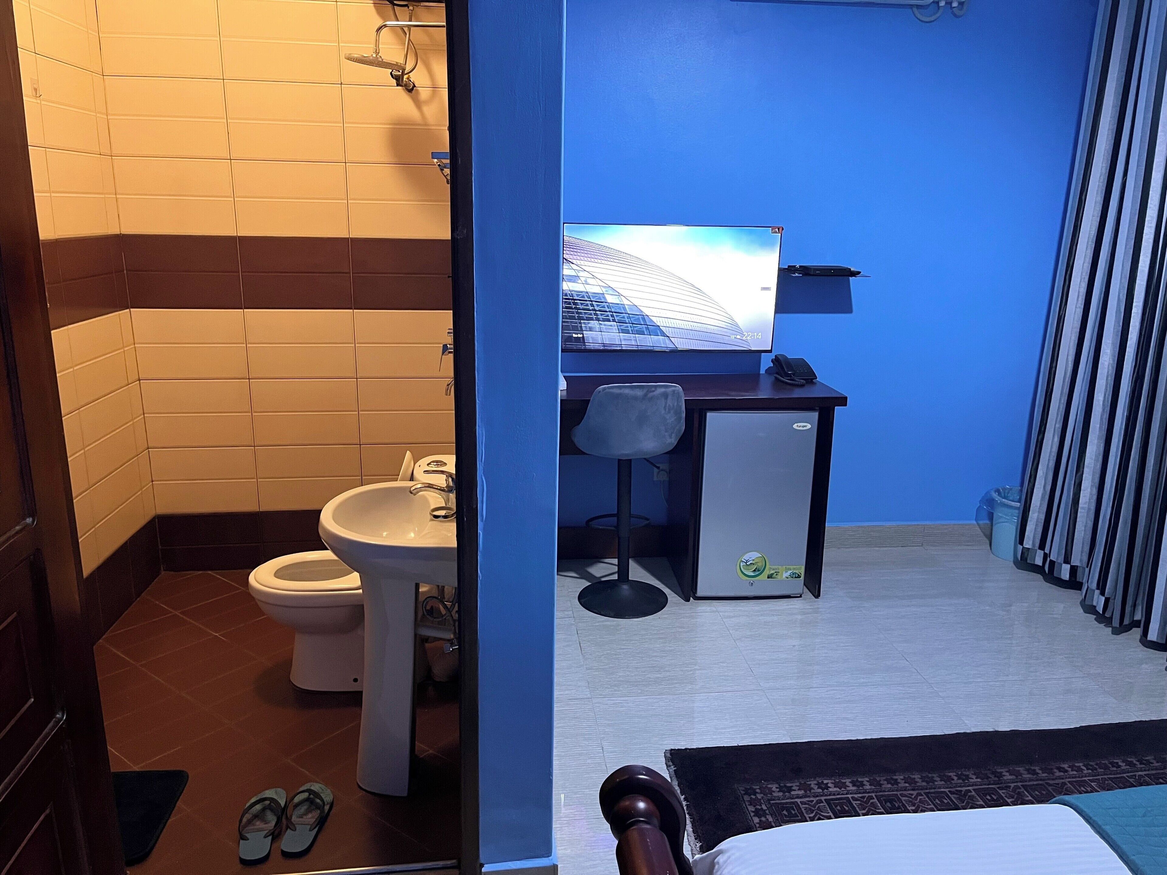 Une petite chambre d’hôtel avec un lit, un bureau avec un ordinateur, un lavabo et des toilettes.