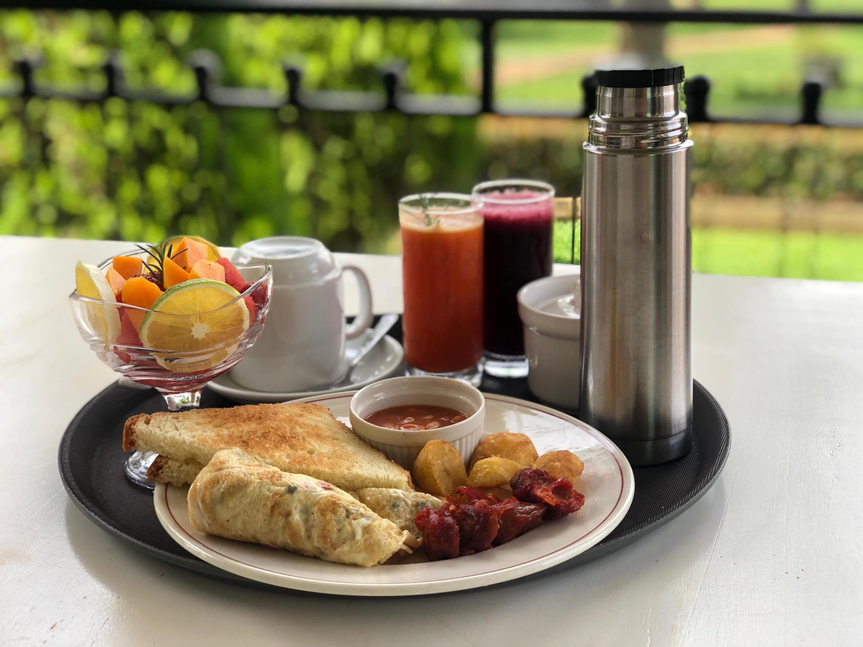 A breakfast tray with eggs, fruit, and beverages on a table with a view of greenery.