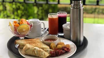 Bandeja de café da manhã com ovos, frutas e bebidas sobre uma mesa com vista para o verde.