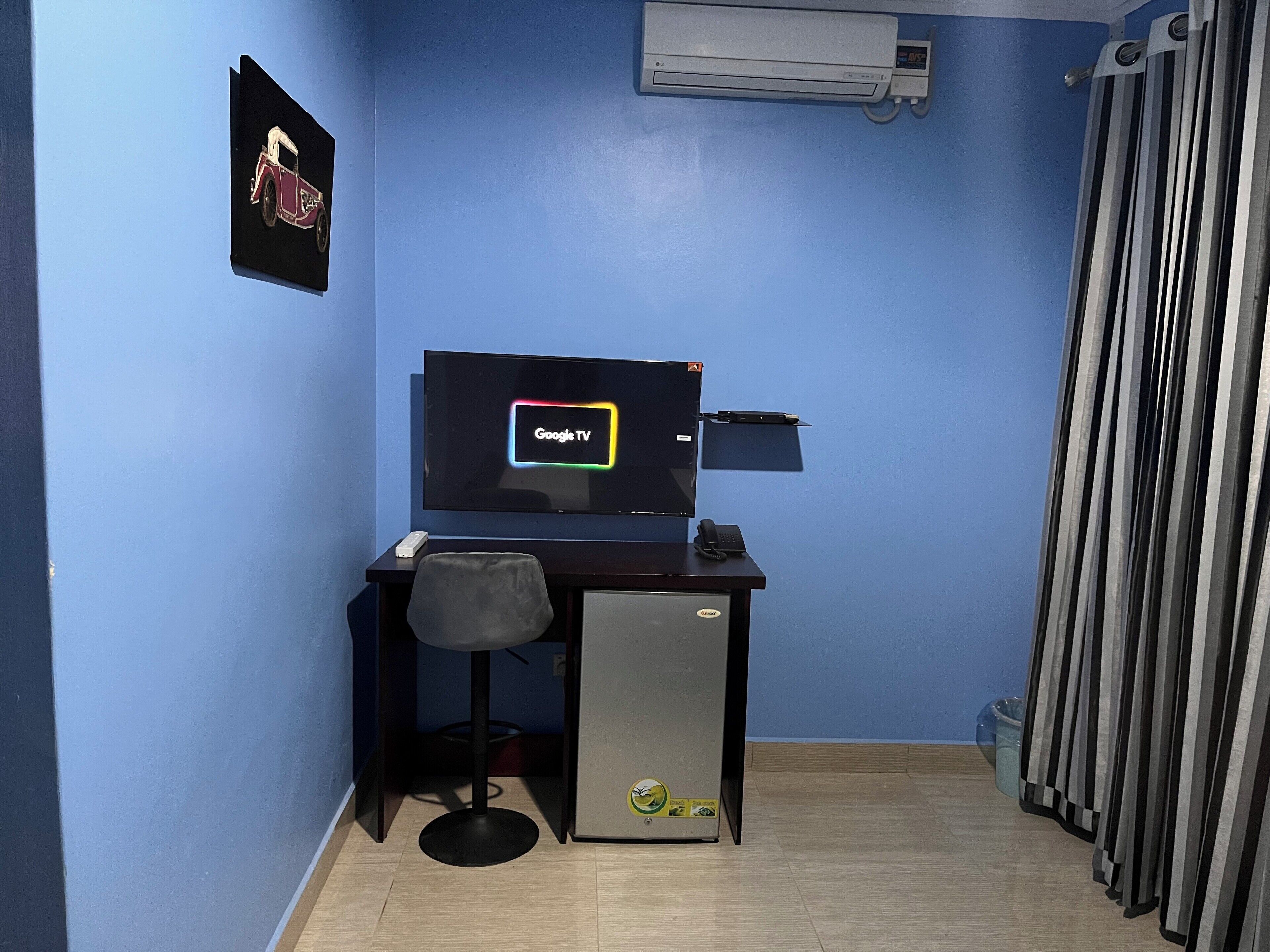 Ein kleiner Büroraum mit Schreibtisch, Stuhl und einem Computerbildschirm, der 'Google TV' anzeigt.