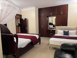 A hotel room with two beds, a wardrobe, a mirror, and a chair. - Lake Point Villa (Entebbe)