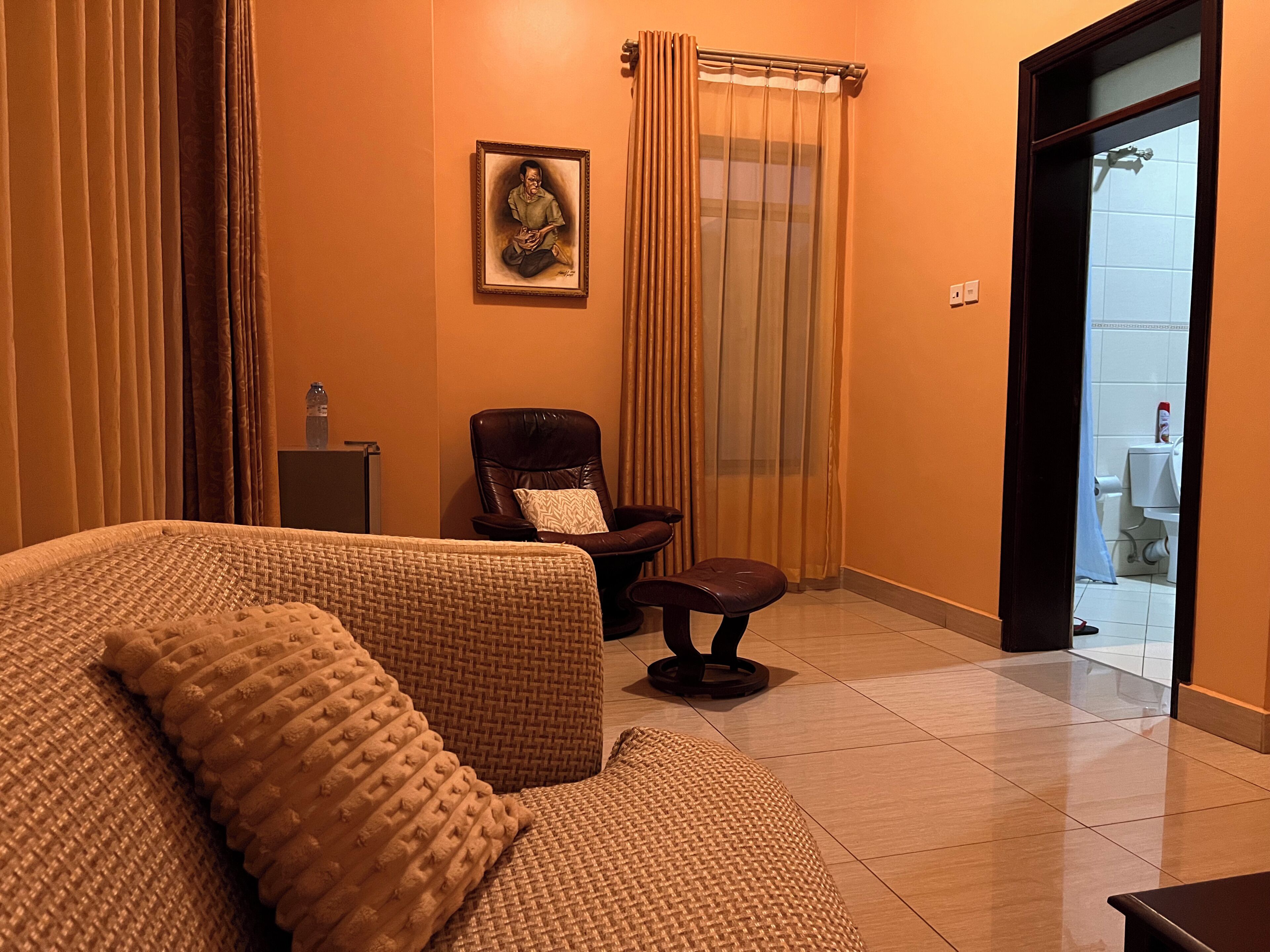 A hotel room with a sofa, a chair, a small table, and a painting on the wall.