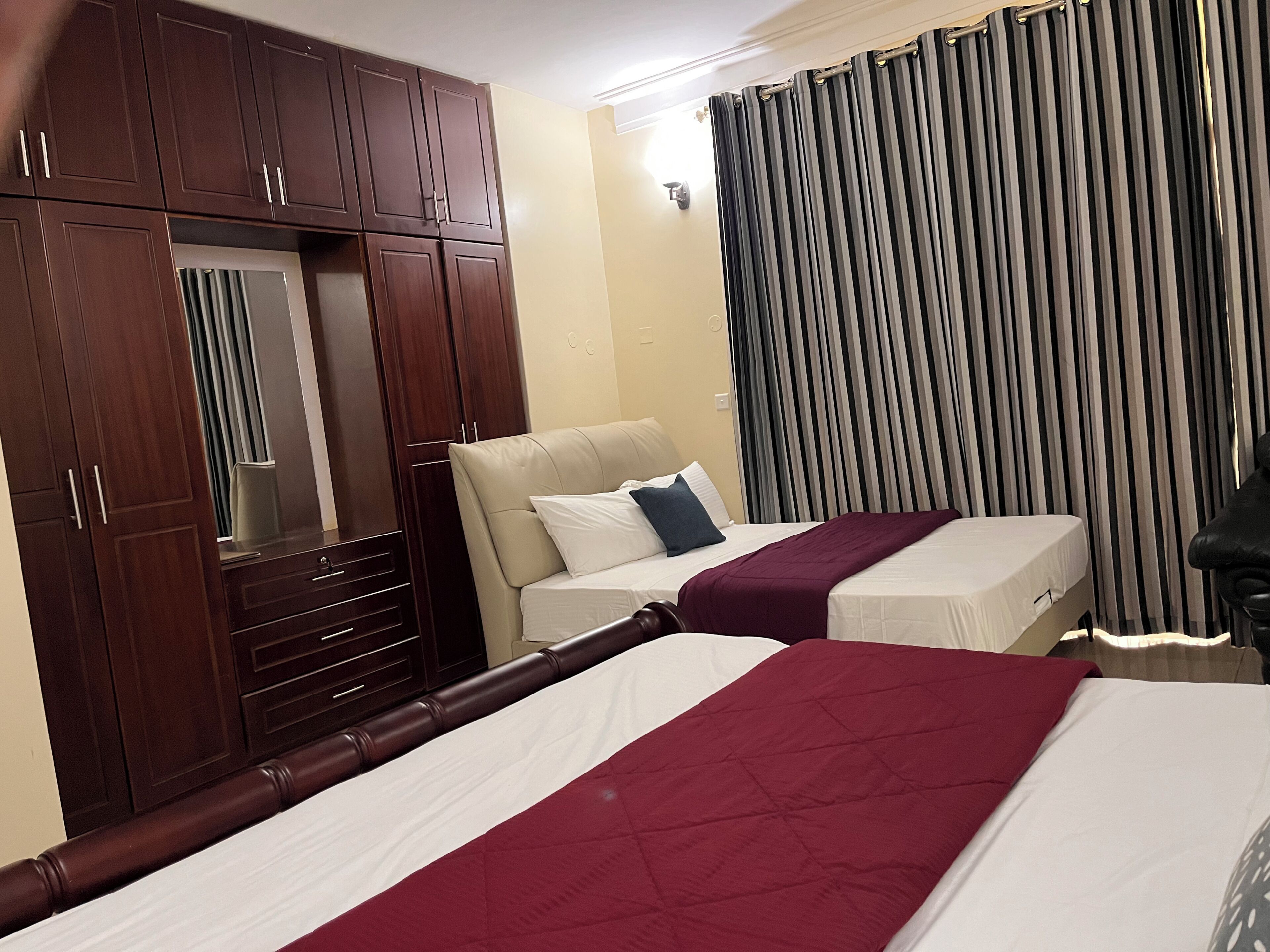 A hotel room with two beds, a wardrobe, a mirror, and a curtain.