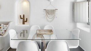 A modern dining area with a glass table, white chairs, a cactus decoration, and a chandelier. - Mellow Luxury Cave (Santorini)